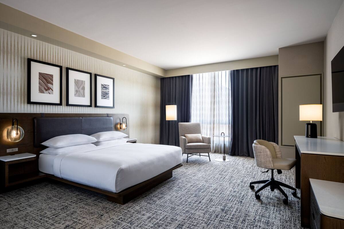 A hotel room with a large bed, a desk, a chair, and a window with curtains.