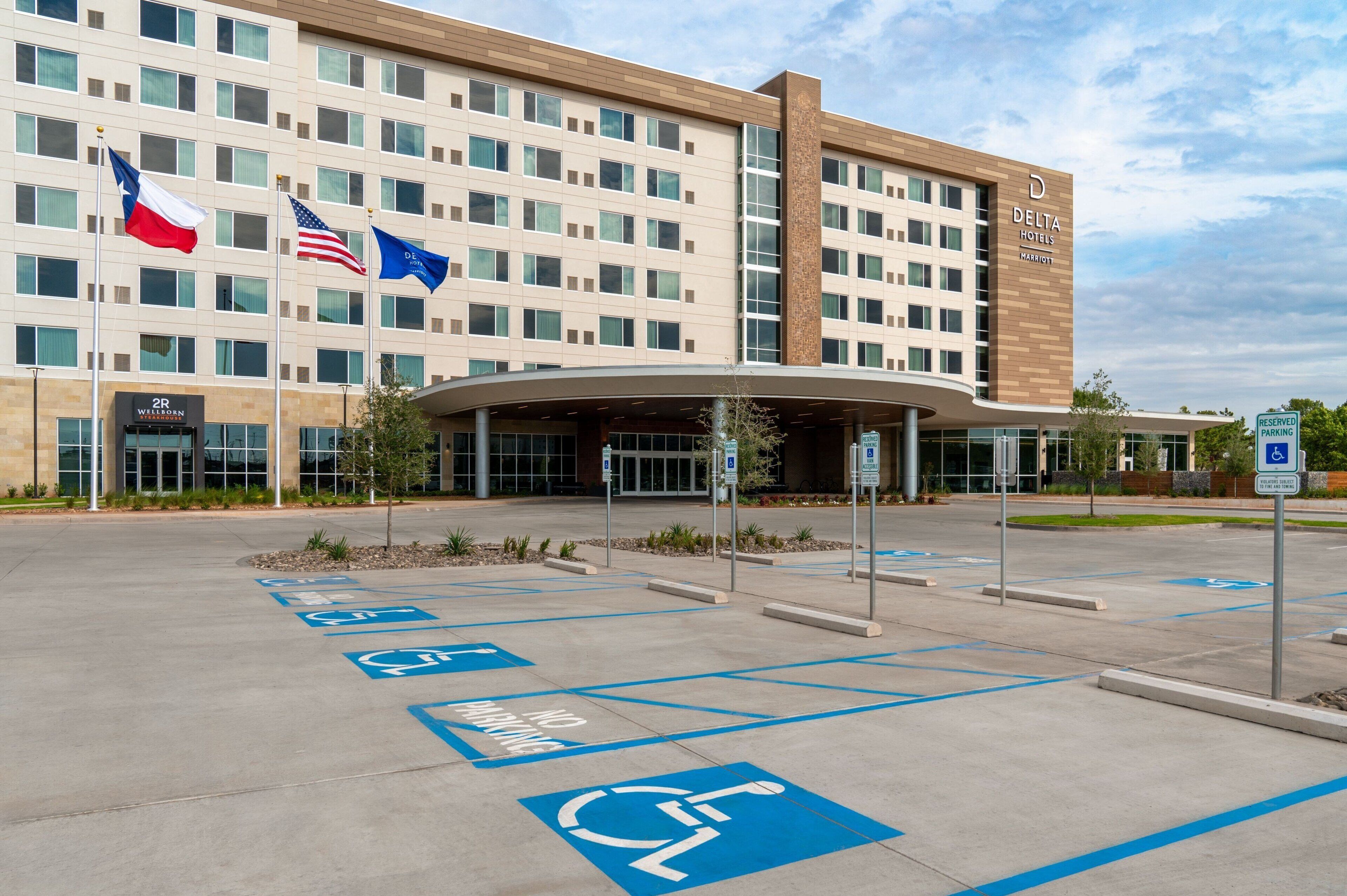A hotel with a modern design, featuring a large parking lot with handicapped accessible spaces and a covered entrance.