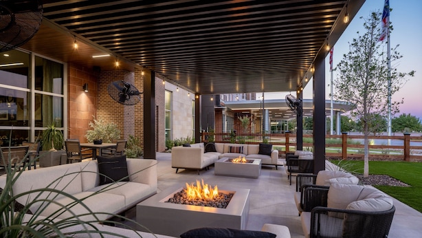 An outdoor patio area with a fire pit, sofas, and chairs, surrounded by a wooden pergola and a brick wall. - Delta Hotels by Marriott Wichita Falls Convention Center (Wichita Falls)
