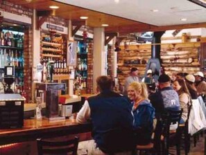 Relax in a rustic bar with a cash register, wooden chairs, and shelves stocked with bottles and glasses.