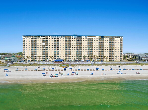 A large hotel with multiple floors and balconies, a beachfront with sun loungers and umbrellas, and a clear blue sky. - Seaside Sunset! Beachside Tiki Hut & More! (Panama City)