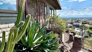 Una casa con vista a un paisaje desértico, un cactus en primer plano y un cielo despejado.