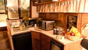 Cocina compacta con microondas, lavamanos y refrigerador pequeño. Hay un armario de madera sobre la encimera y una ventana con cortinas.