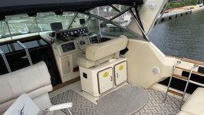Interior de un barco con una cabina de control, asientos acolchados y armarios de almacenamiento.