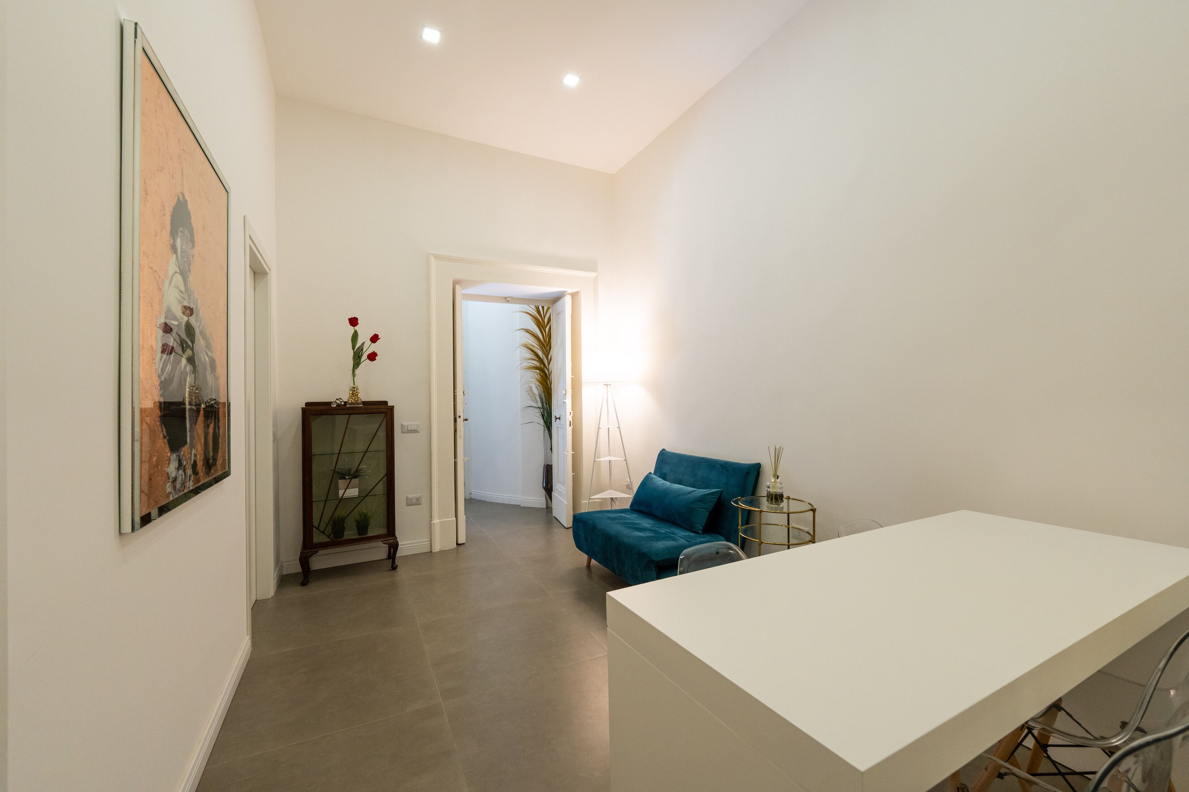 A modern room with a white desk, a blue sofa, and a framed artwork on the wall.