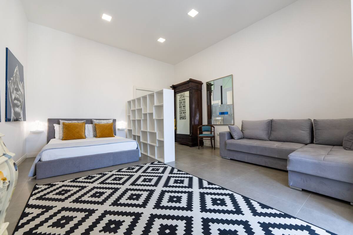 Ein modernes Schlafzimmer mit einem Bett, einem grauen Sofa und einem gemusterten Teppich.
