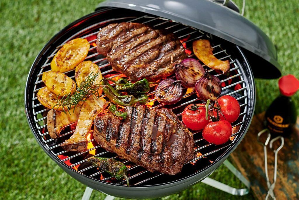 Een barbecue met steaks, aardappelen, uien en tomaten.