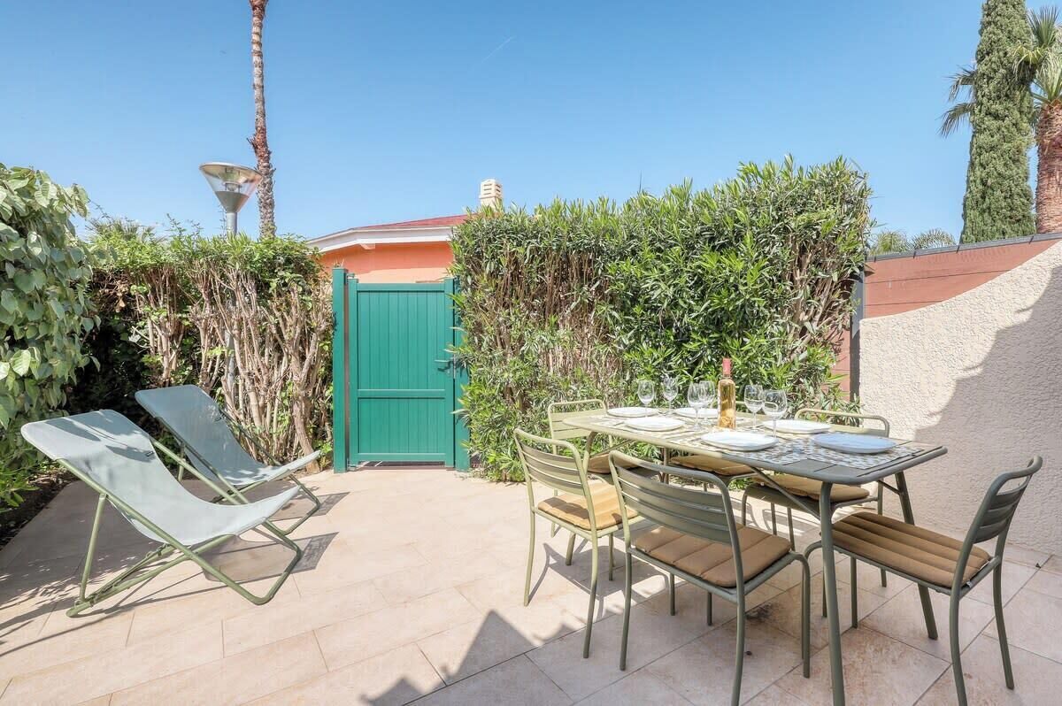 Un patio al aire libre con una mesa lista para comer, rodeado de sillas y una puerta verde.