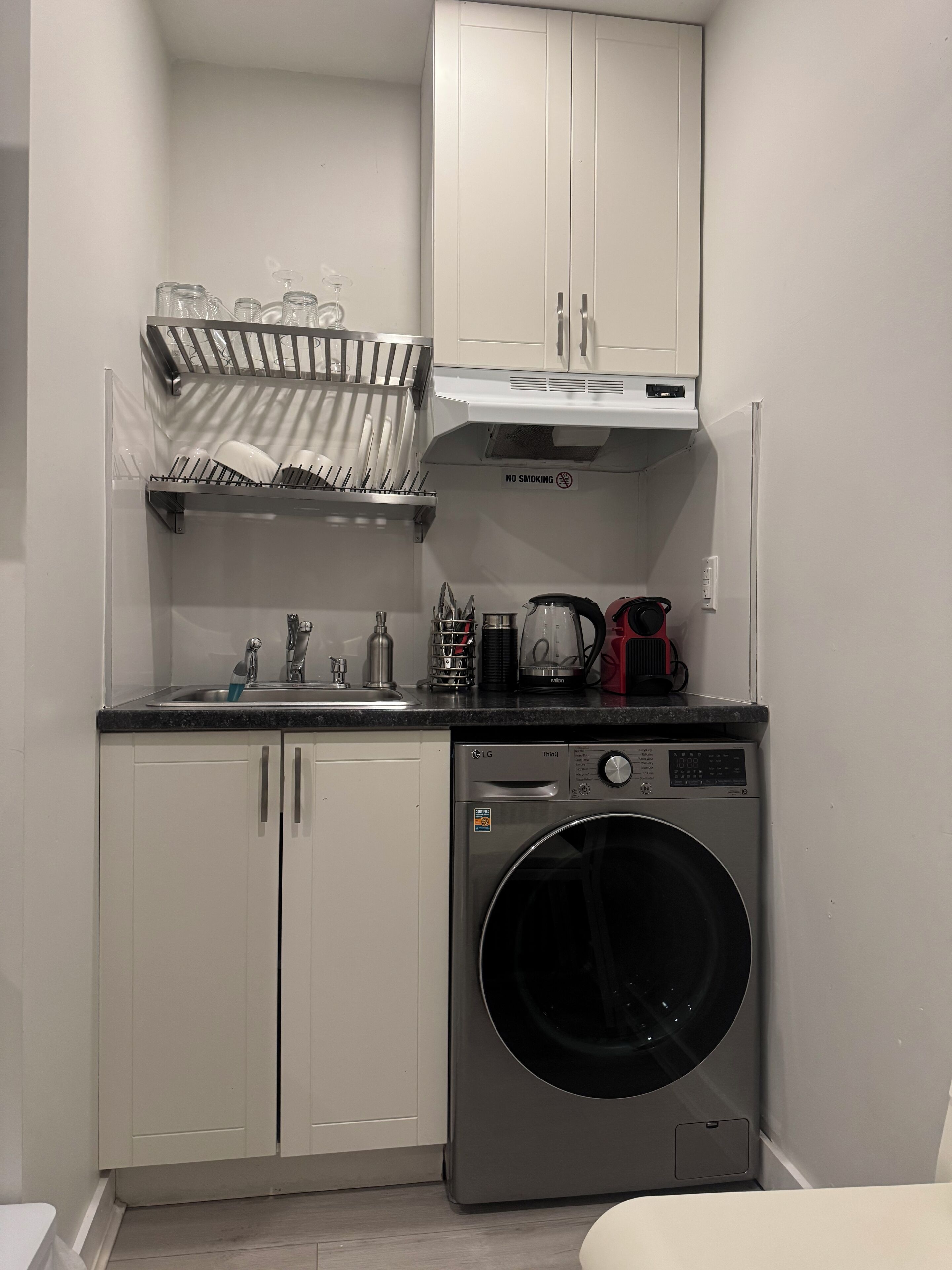 Cocina compacta con lavadora integrada, un escurreplatos y cafetera.