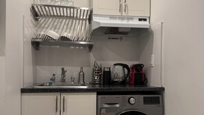 Cocina compacta con lavadora integrada, un escurreplatos y cafetera.