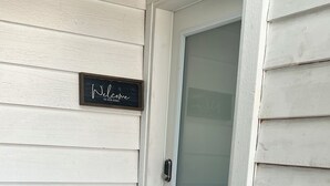 Una puerta blanca con un panel de vidrio esmerilado, un letrero de bienvenida negro y un felpudo a rayas.