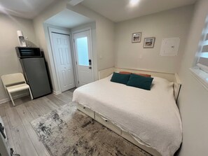 A bedroom with a bed, a chair, a refrigerator, and a door. - Cozy Guest Suite in Edgemont Village (North Vancouver)