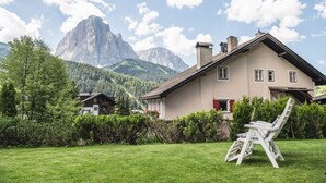 Uma casa com telhado inclinado, chaminé e jardim com gramado e uma cadeira.