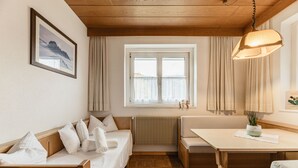Um quarto acolhedor com teto de madeira, janela com cortinas, cama com almofadas, mesa com uma planta e radiador.