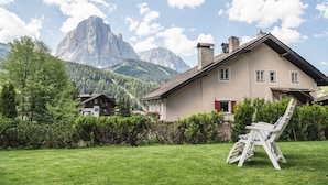 Una casa con techo inclinado, chimenea y jardín con césped y una silla.