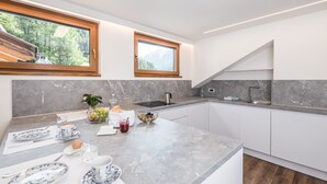 Eine moderne Küche mit Marmorarbeitsplatten, weißen Schränken und zwei Fenstern mit Blick ins Freie.