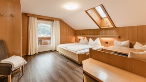 Ein Schlafzimmer mit Holzboden, einem Bett mit weißer Bettwäsche, einem Schreibtisch, einem Stuhl und einem Fenster mit Vorhängen.