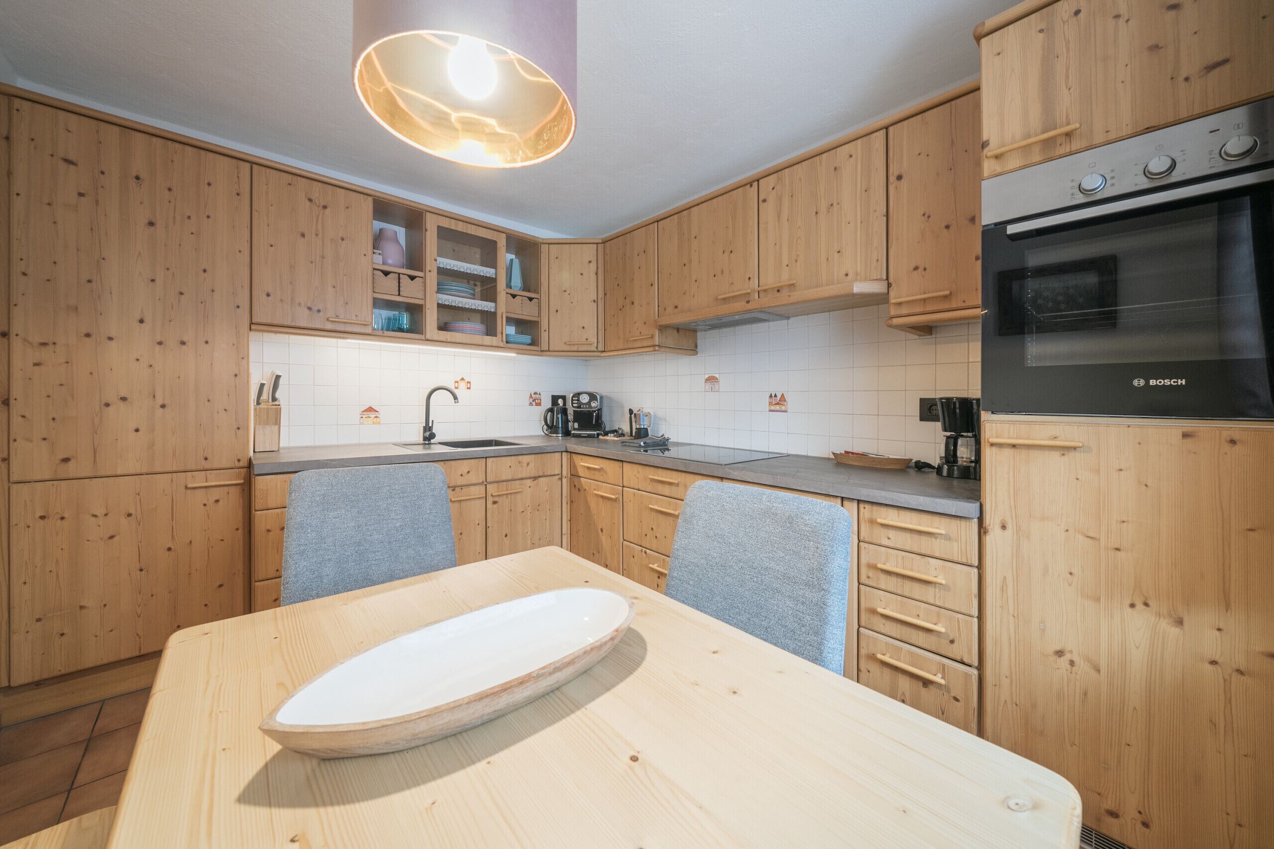 A modern kitchen with wooden cabinets, a Bosch oven, and a dining table with a white oval centerpiece.
