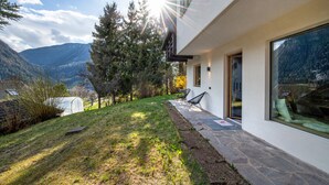 A modern house with a stone pathway leading to a glass door, surrounded by a well-maintained lawn and trees. - 191A Apartments Elmarino (Ortisei)