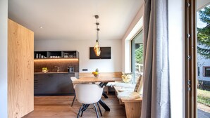 A modern kitchen with a wooden countertop, a dining area with a table and chairs, and a large window with curtains. - 191A Apartments Elmarino (Ortisei)