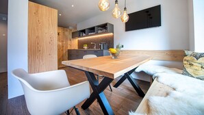 A modern dining area with a wooden table, white chairs, and a fur-covered bench. - 191A Apartments Elmarino (Ortisei)