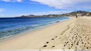 A beach with footprints leading to the water, a clear sky, and distant hills. - Las Mananitas-Awesome Luxury Beachside Condo in Cabo! (San José del Cabo)