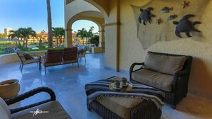 A spacious outdoor seating area with wicker furniture and a view of palm trees and buildings. - Las Mananitas-Awesome Luxury Beachside Condo in Cabo! (San José del Cabo)