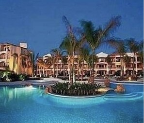 Un complexe hôtelier doté d’une grande piscine, entourée de palmiers et bordée d’immeubles à plusieurs étages.