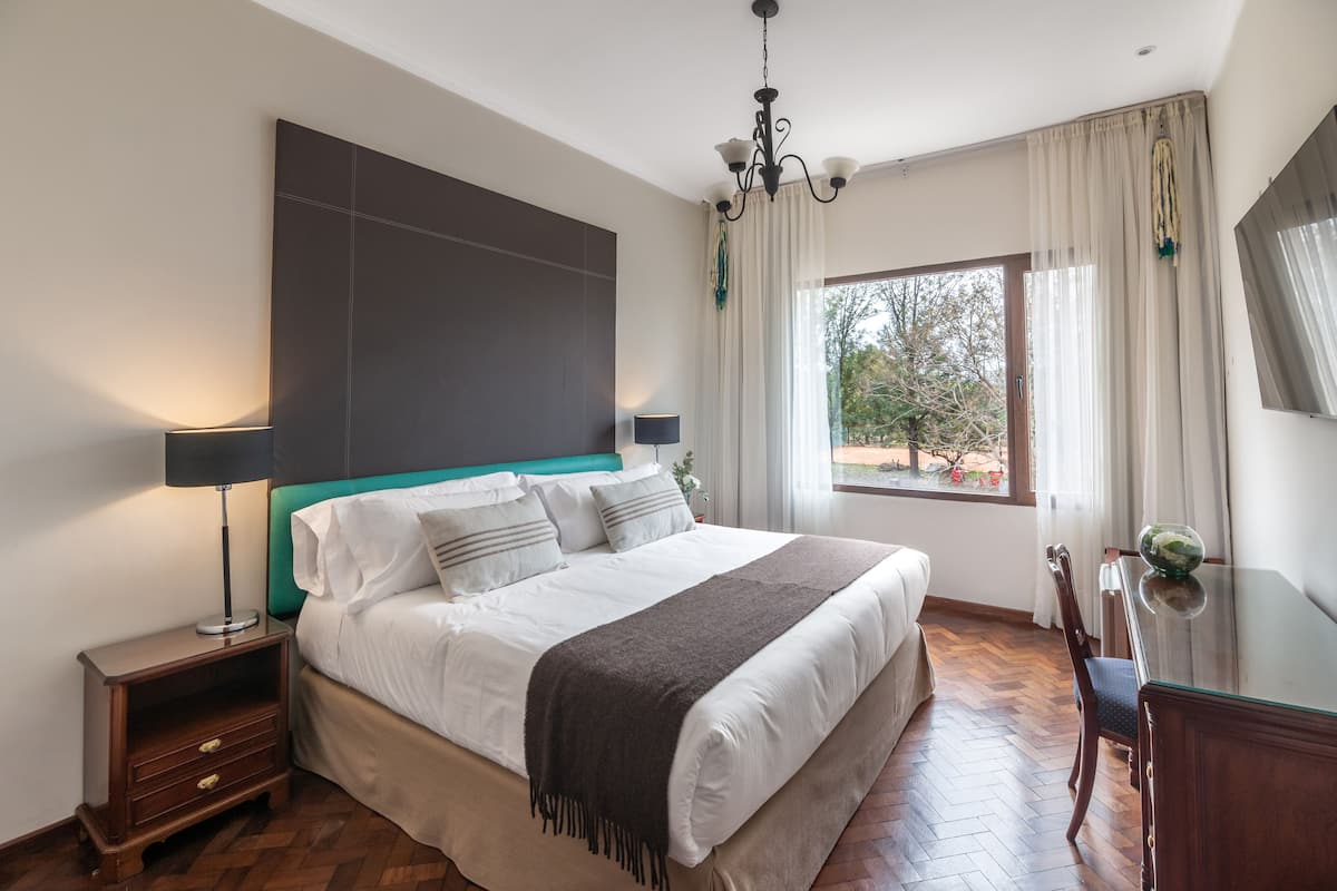 Une chambre à coucher moderne avec un grand lit, des tables de chevet, un bureau et une vue sur l’extérieur.