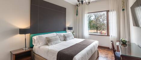 Un dormitorio moderno con una cama grande, mesitas de noche, un escritorio y vistas al exterior.