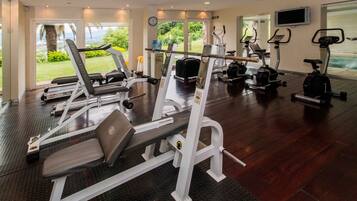 Et fitnesscenter med løbebånd, styrketræningsudstyr og et fjernsyn på væggen.