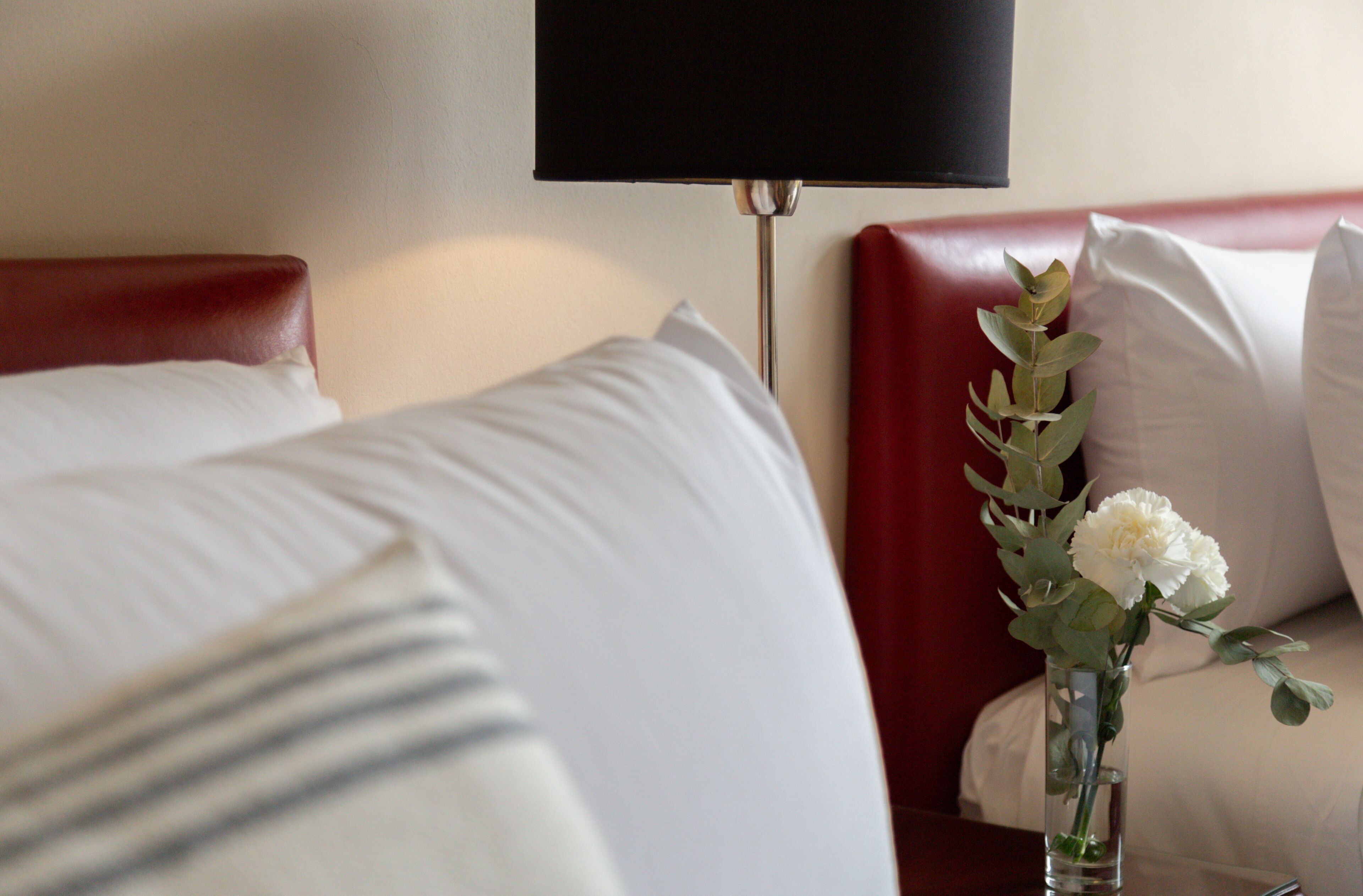 Una habitación de hotel con cama, mesita de noche, un jarrón con flores y una lámpara.