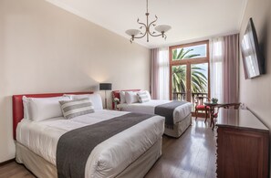 Ein Hotelzimmer mit zwei Betten, einem Fernseher, einer Kristallleuchtre und einem Balkon mit Blick auf Palmen.