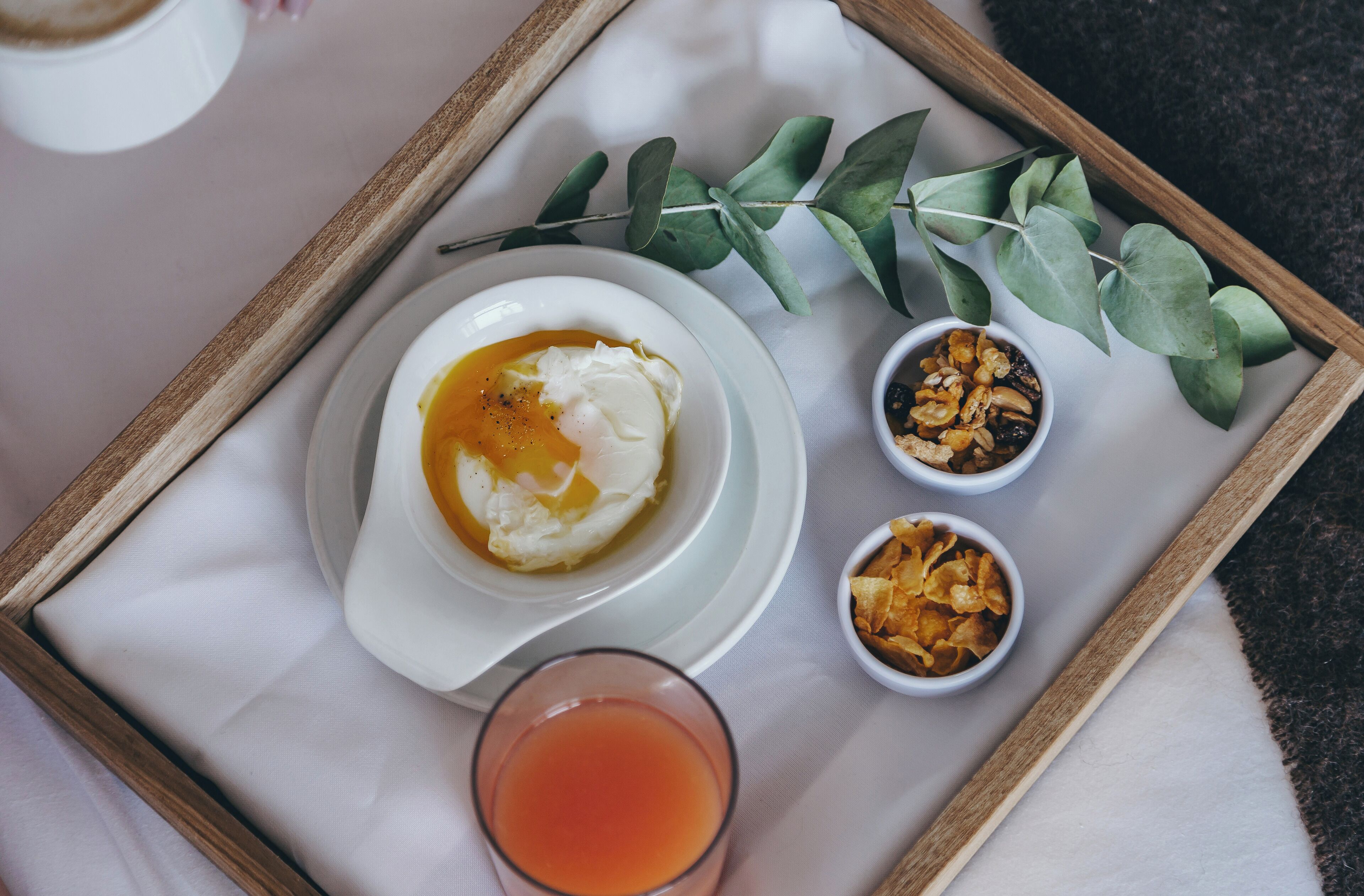 Una bandeja con un tazón de yogur cubierto de miel, dos recipientes pequeños de nueces y un vaso de jugo.