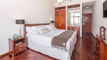 A neatly arranged bedroom with a large bed, wooden wardrobe, and a television on the wall.