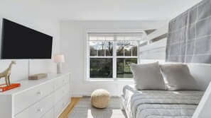 Een moderne slaapkamer met een bed, een televisie, een dressoir en een raam met uitzicht op bomen.