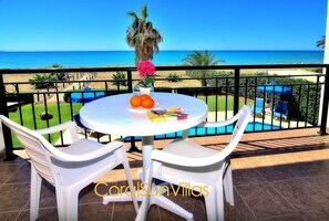 Enjoy the ocean view from this villa's balcony, featuring a table for two, a vase with a single flower, and a fruit platter.