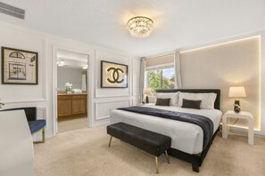 Ein Schlafzimmer mit einem großen Bett, einer Bank, einem Nachttisch, einer Chandelüster und gerahmten Kunstwerken.