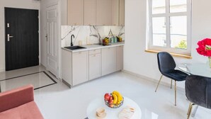 Une cuisine moderne avec des armoires blanches, un pare-feu en marbre et un évier noir. On y trouve également un coin repas avec une table ronde et une chaise noire.