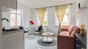 Un salon moderne et bien éclairé, avec un coin cuisine, une table basse ronde et un canapé rose.