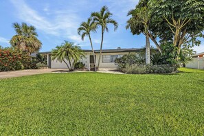 A house with a well-maintained lawn, palm trees, and a clear sky.