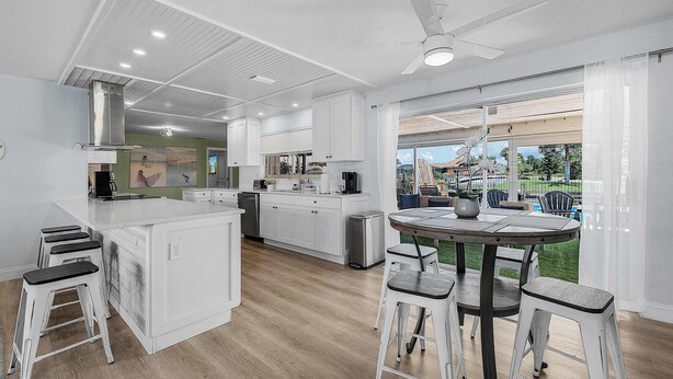 A modern kitchen with a central island, bar stools, and a dining table with chairs.