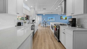 A modern kitchen with white cabinetry, a wooden floor, a dining area with a table and chairs, and a ceiling fan.