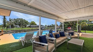 An outdoor patio with a pool, lounge chairs, and a covered seating area.