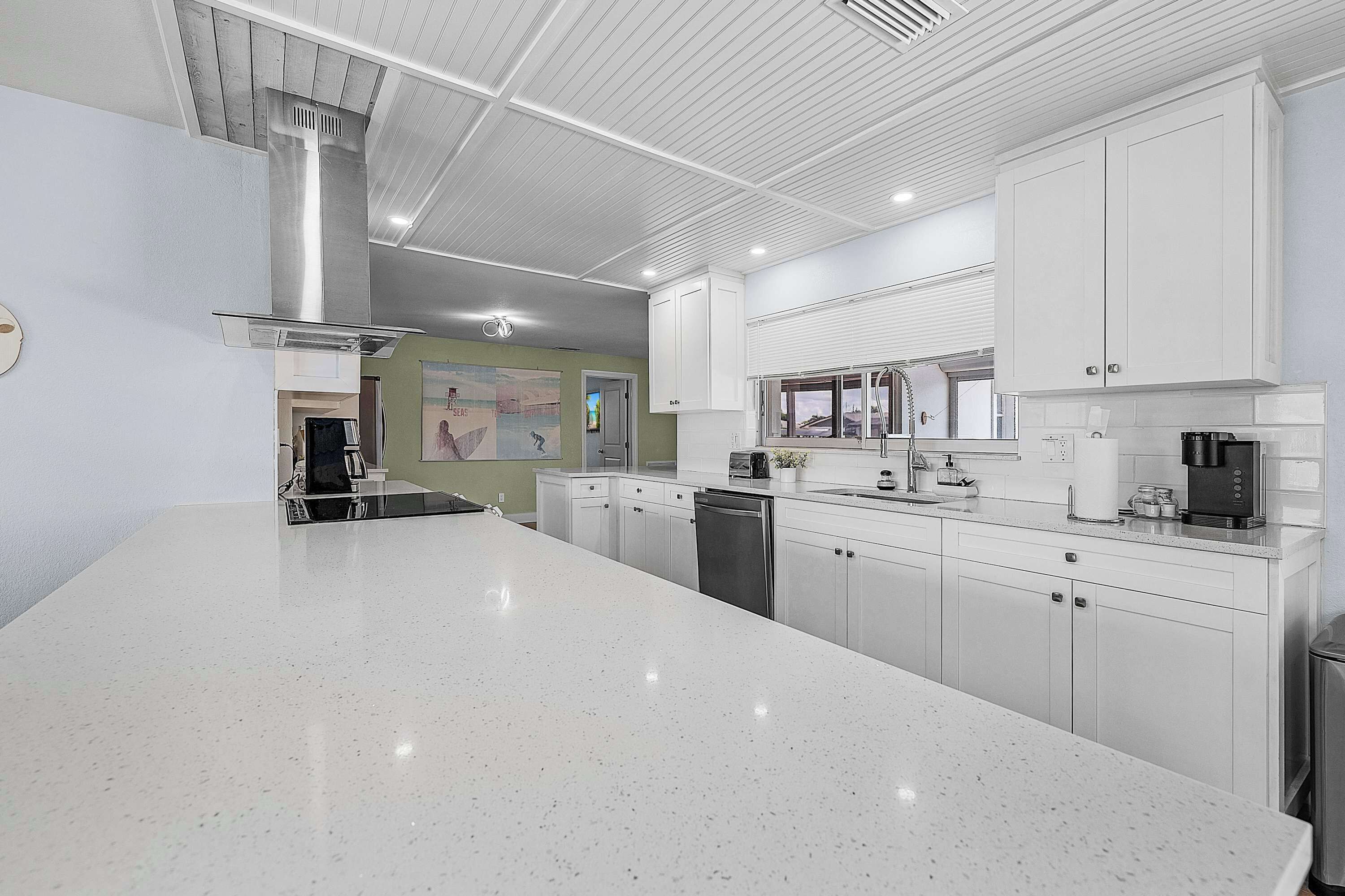 A modern kitchen with white cabinetry, a stainless steel range hood, and a large island.
