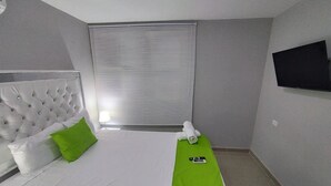 A hotel room with a bed, a green bedside table, a TV on the wall, and a window with blinds. - Room-bm-14 Room Near the sea With air co (Cartagena)