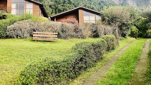 Dos cabañas de madera con ventanas amplias, rodeadas de abundante vegetación y un paisaje montañoso.
