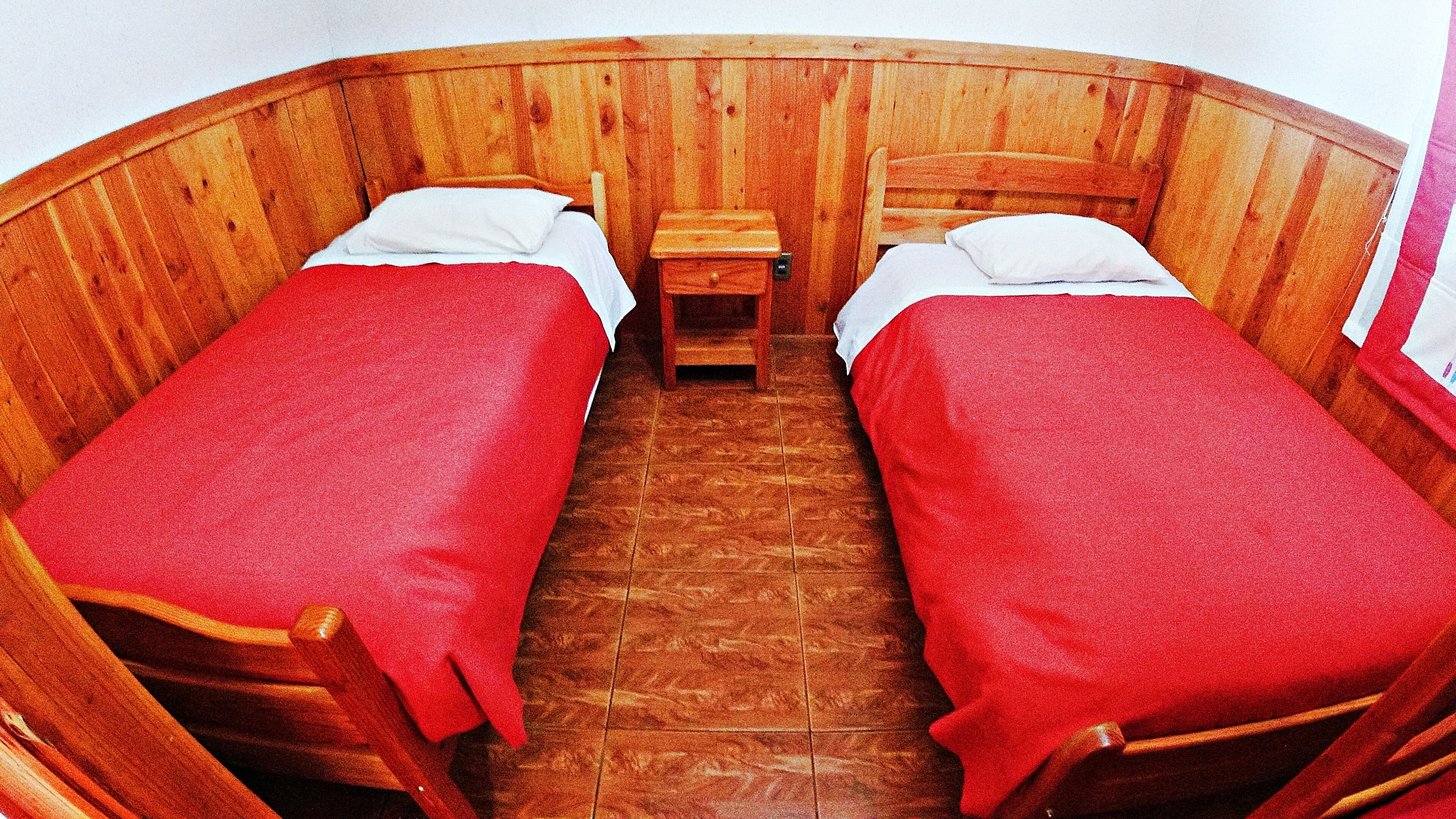 Une cabane en bois avec deux lits simples, chacun étant équipé d’une couverture rouge et d’un oreiller blanc.