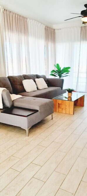 A modern living room with a sectional sofa, a glass coffee table, and a ceiling fan. - Spacious full equip Villa w/ocean view A (Willemstad)