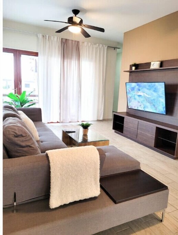 A modern living room with a sofa, a coffee table, a TV mounted on the wall, and a ceiling fan.